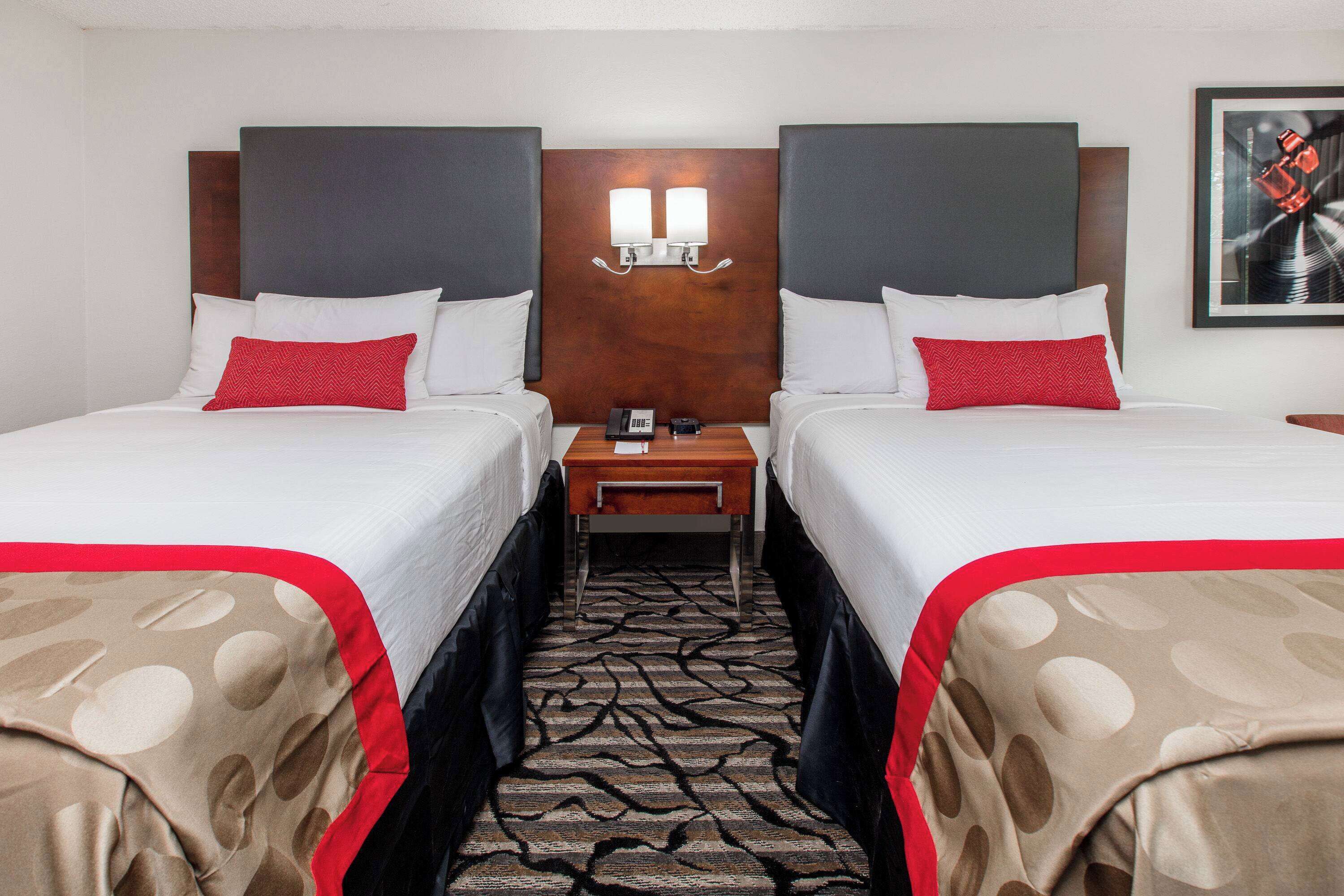 A hotel room with two beds, a nightstand, and a headboard with wall-mounted lights.