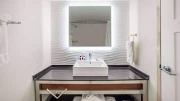 Un baño moderno con un lavamanos con recinto de vidrio, un perchero y un espejo sobre el lavamanos.