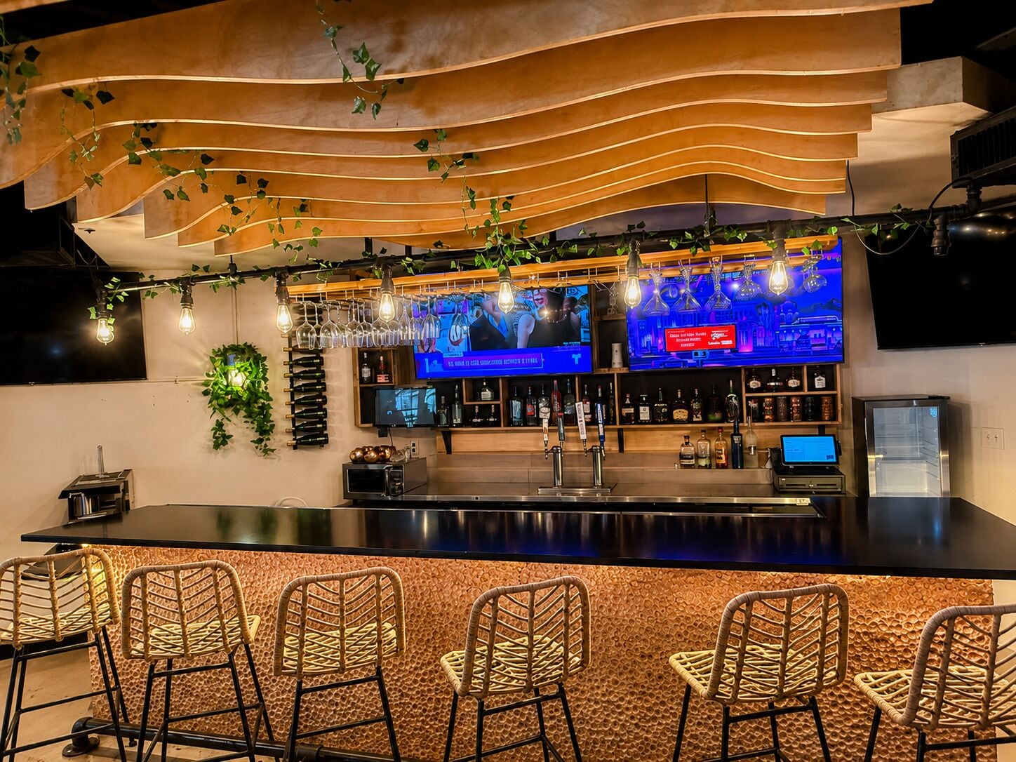 Uma área de bar com balcão extenso, várias televisões e banquetas.