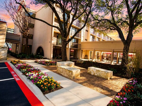 A modern building with a fire lane, outdoor seating, and a landscaped garden. - Ramada by Wyndham Austin South (Austin)