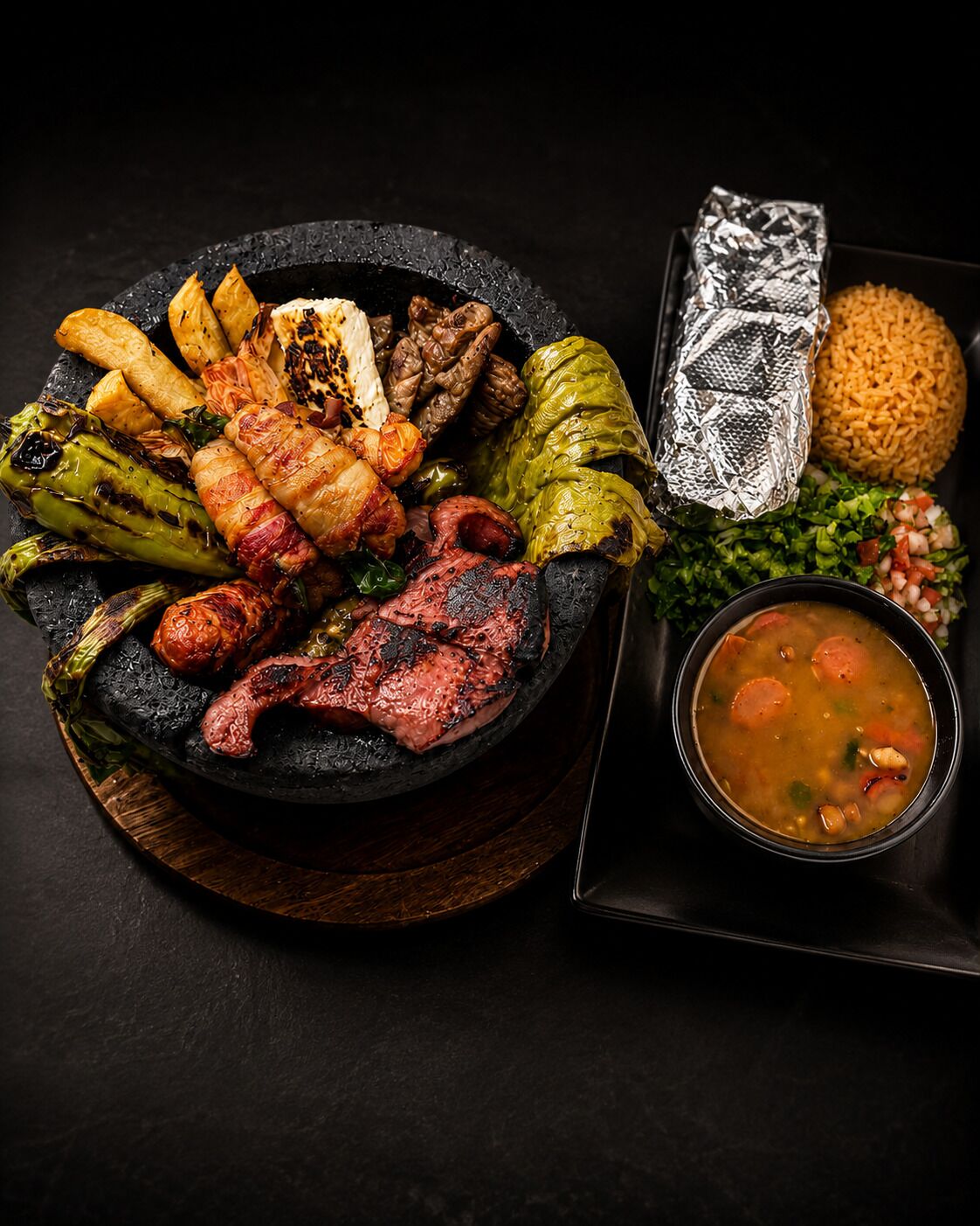 Variedad de carnes a la parrilla y verduras sobre una fuente de piedra, acompañadas de arroz y un tazón de sopa.