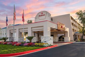 A Ramada hotel with a modern design, featuring a prominent entrance, a landscaped garden, and multiple flags.