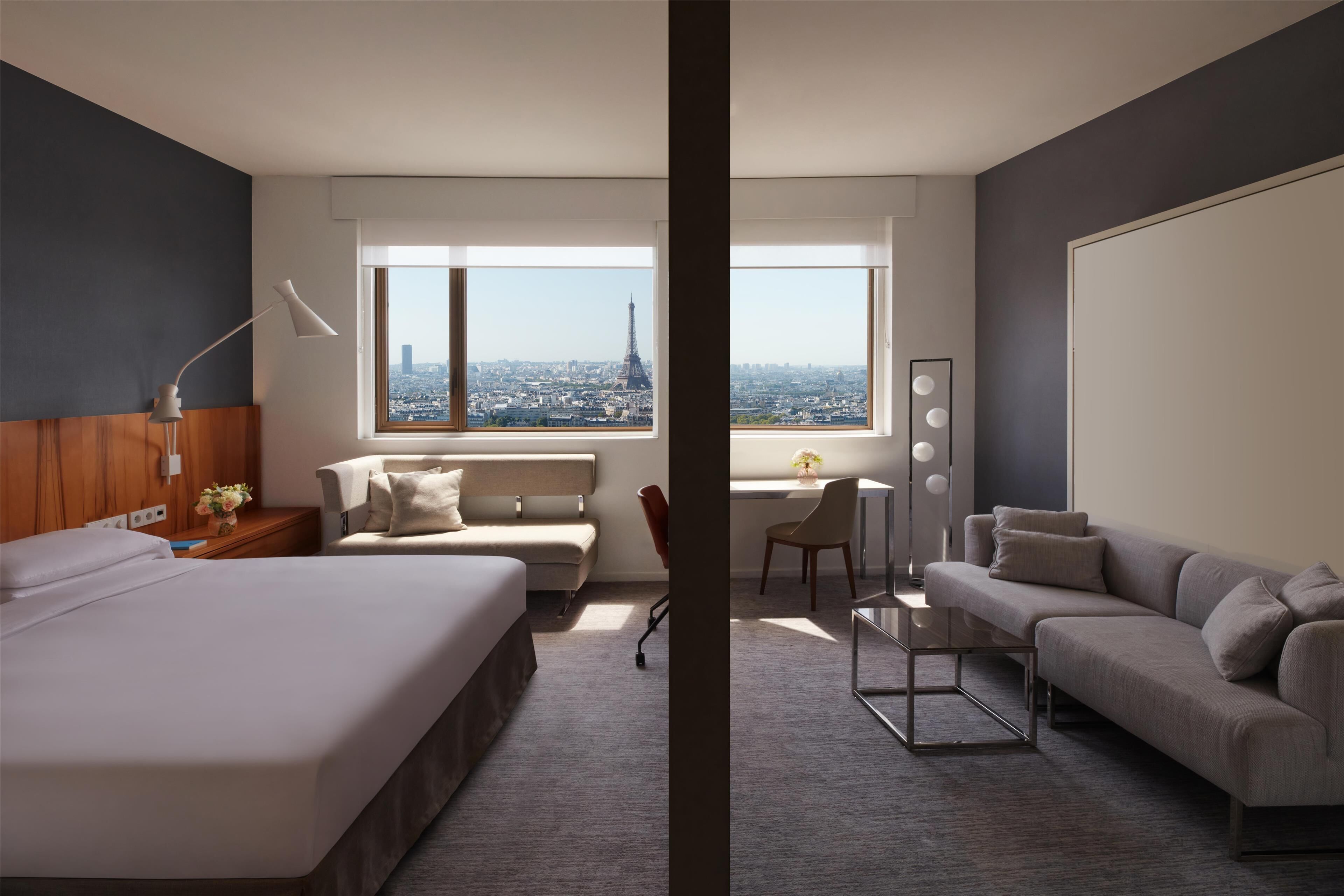 Una habitación de hotel moderna con una cama grande, un sofá, un escritorio con una silla y vistas a la Torre Eiffel.