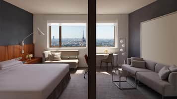 Una habitación de hotel moderna con una cama grande, un sofá, un escritorio con una silla y vistas a la Torre Eiffel.