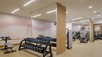 Een sportschool met gewichthefapparatuur, cardioapparaten en een grote spiegel.