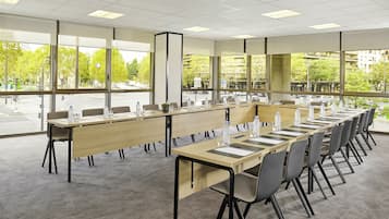 A conference room with a long table, chairs, and large windows offering a view of the street and trees.