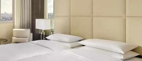 A hotel room with a large bed, a chair, a lamp, and a view of the city through a window.