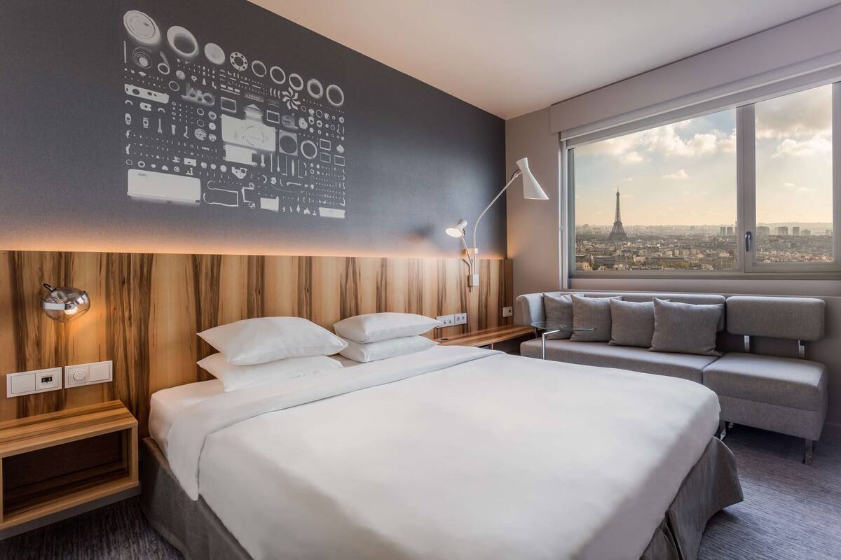 Moderni hotellihuone, jossa on suuri sänky, oleskelualue, näkymä kaupunkiin ja seinä, jonka kuvioinnissa on käytetty piirilevyaihetta.