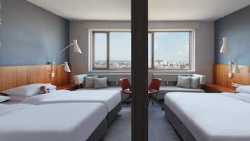 A hotel room with two beds, a sofa, a chair, and a large window offering a city view.