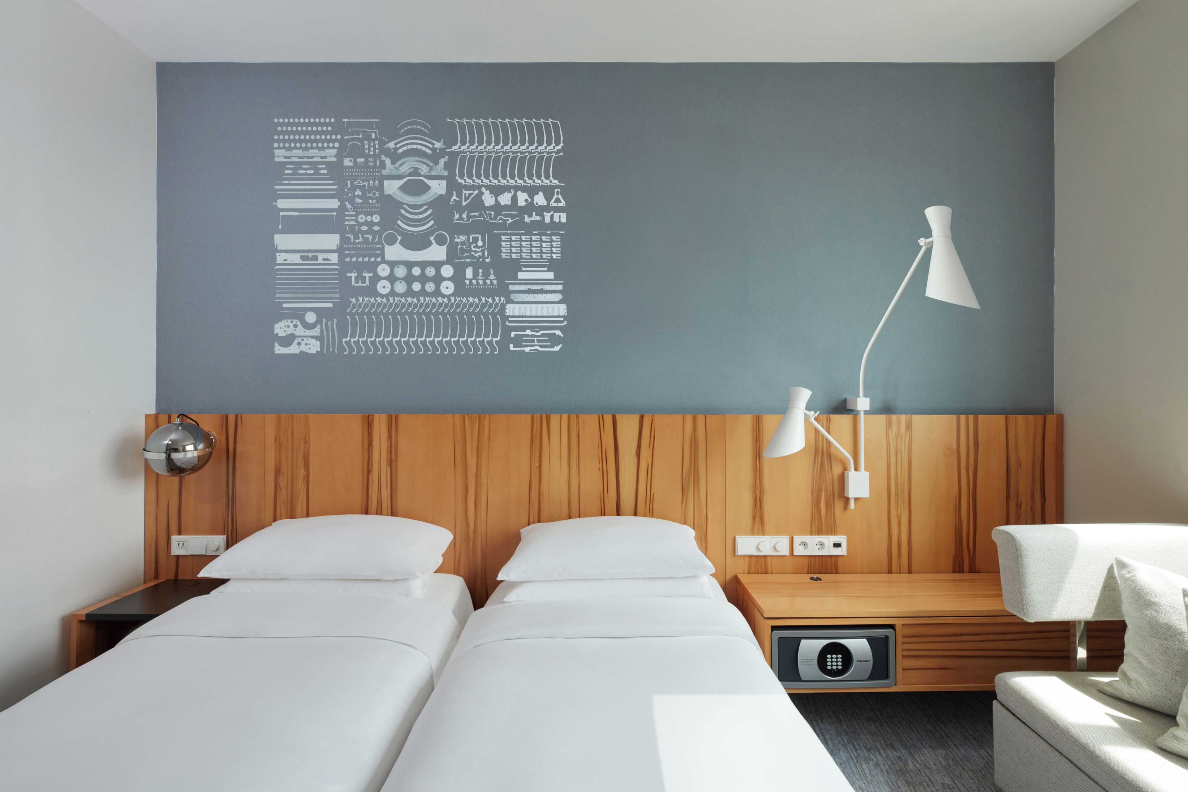 Een hotelkamer met twee bedden, een houten hoofdbord, een wandlamp en een kunstwerk aan de muur.