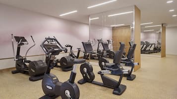 Une salle de sport équipée de plusieurs appareils de cardio, dotée d’un mur avec des miroirs et d’une colonne en bois.