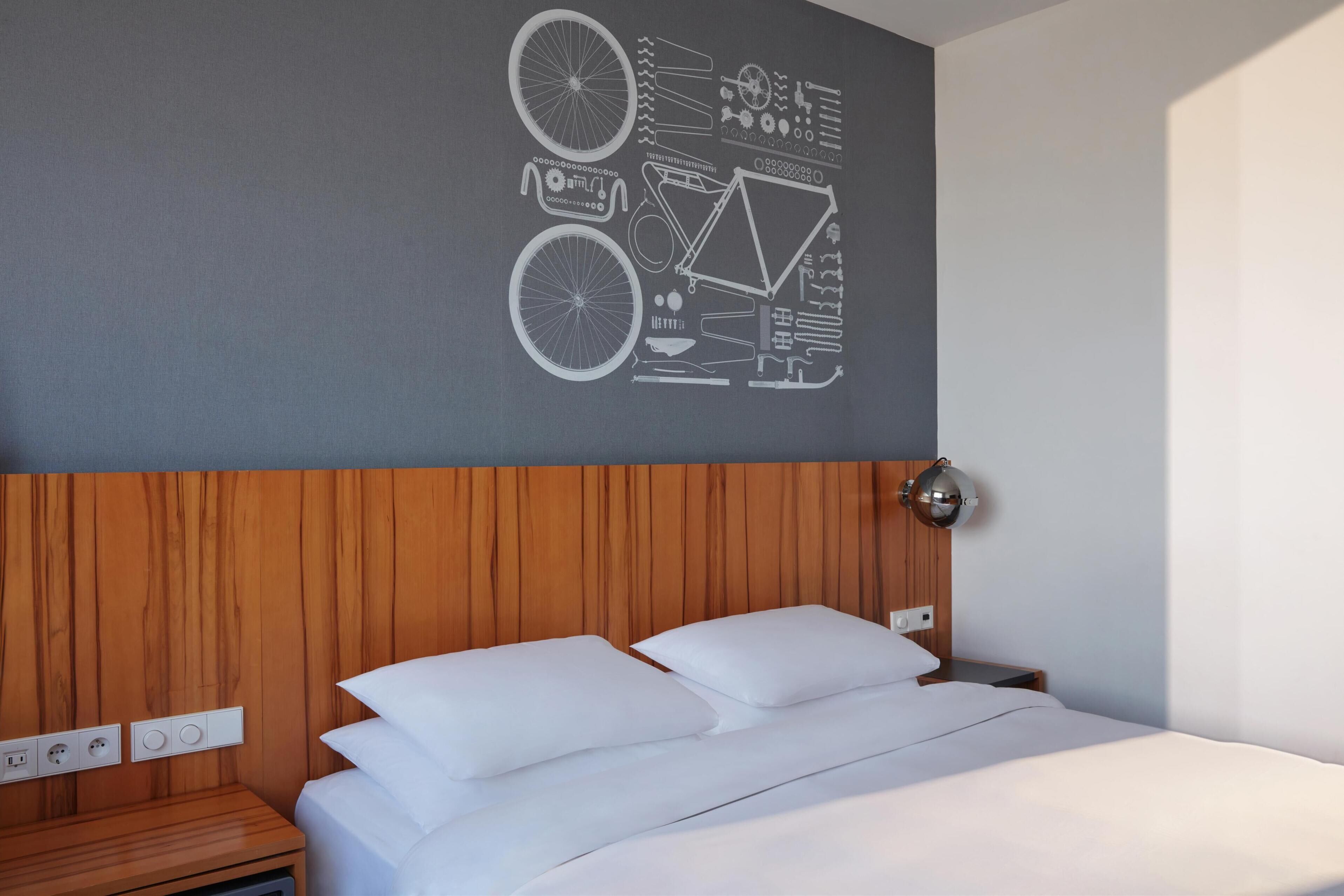 Una cama bien hecha con sábanas y almohadas blancas, un cabecero de madera y una pared con diseño geométrico.