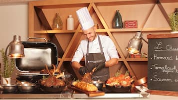 Un chef prépare des plats dans une cuisine où un tableau noir affiche le menu, avec des plats tels que « homard », « tomaquard » et « saumon ».