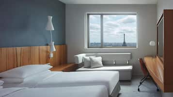 A hotel room with two beds, a desk, a chair, a lamp, and a large window with a view of the Eiffel Tower.