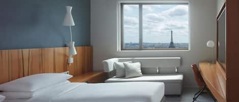 A hotel room with two beds, a desk, a chair, a lamp, and a large window with a view of the Eiffel Tower.
