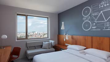 A hotel room with a large window, a bed, a desk, and a wall with a bicycle-themed design.