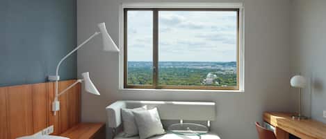 Habitación de hotel moderna con cama, escritorio, silla, ventana y vista a la ciudad, además de una lámpara.