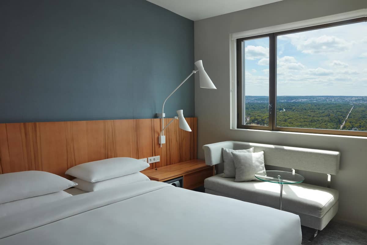 Hotellihuone, jossa on suuri ikkuna, sänky, sohva, työpöytä ja lamppu.