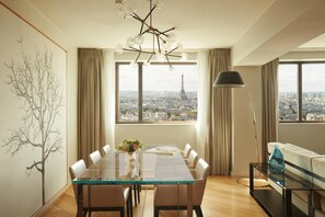 A dining area with a glass table, chairs, a vase of flowers, and a view of the Eiffel Tower through large windows. - Hyatt Regency Paris Etoile (Paris)