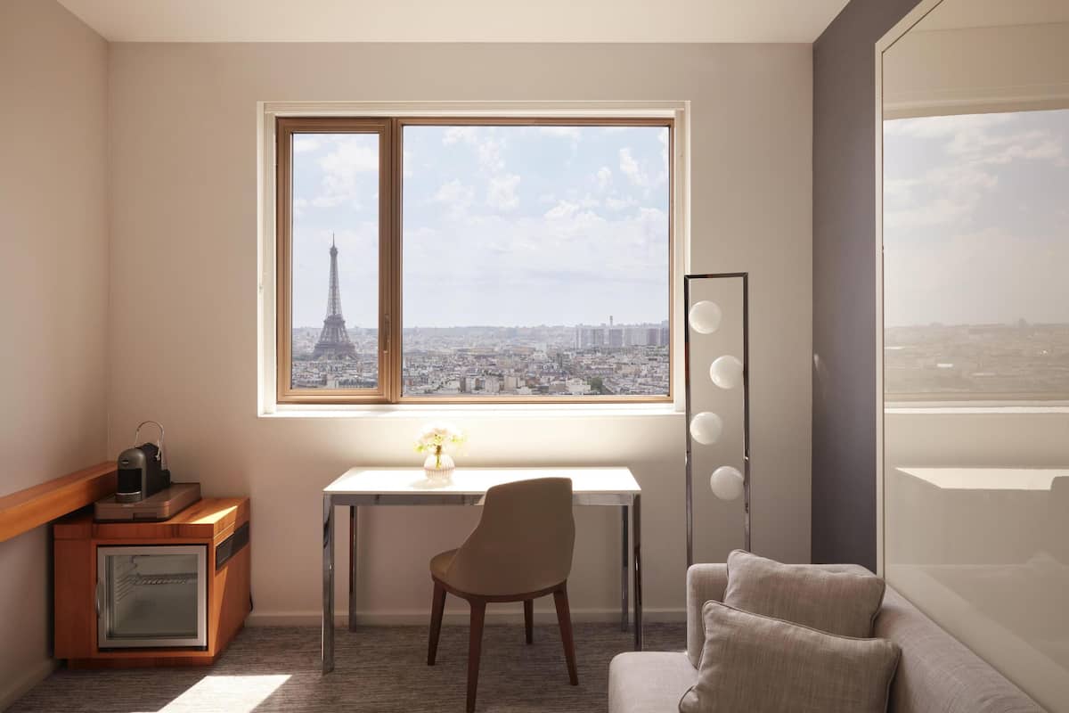 Huone, josta on näkymä Eiffel-tornille, työpöytä tuolilla, pieni kaappi ja lattiavalaisin.