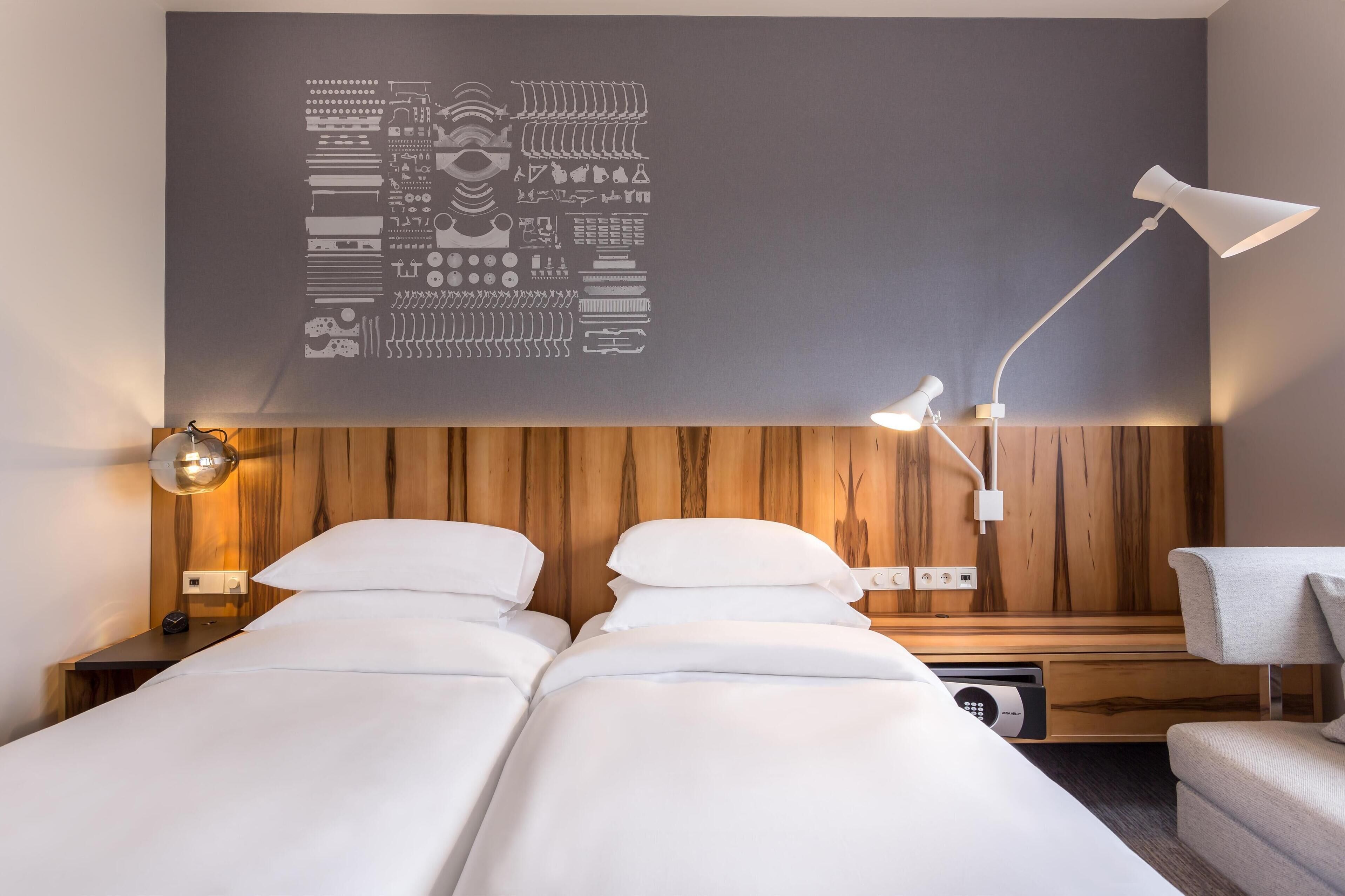A hotel room with a wooden headboard, a bed with white linens, a bedside table with a lamp, and a wall art piece.