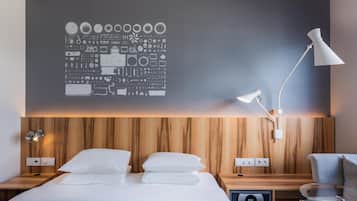 A modern hotel room with a wooden headboard, a large wall art piece, a bedside table with a lamp, and a glass coffee table.