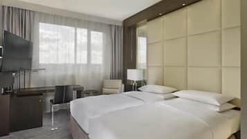 A hotel room with a large bed, a desk with a chair, a TV, and a large window with curtains.