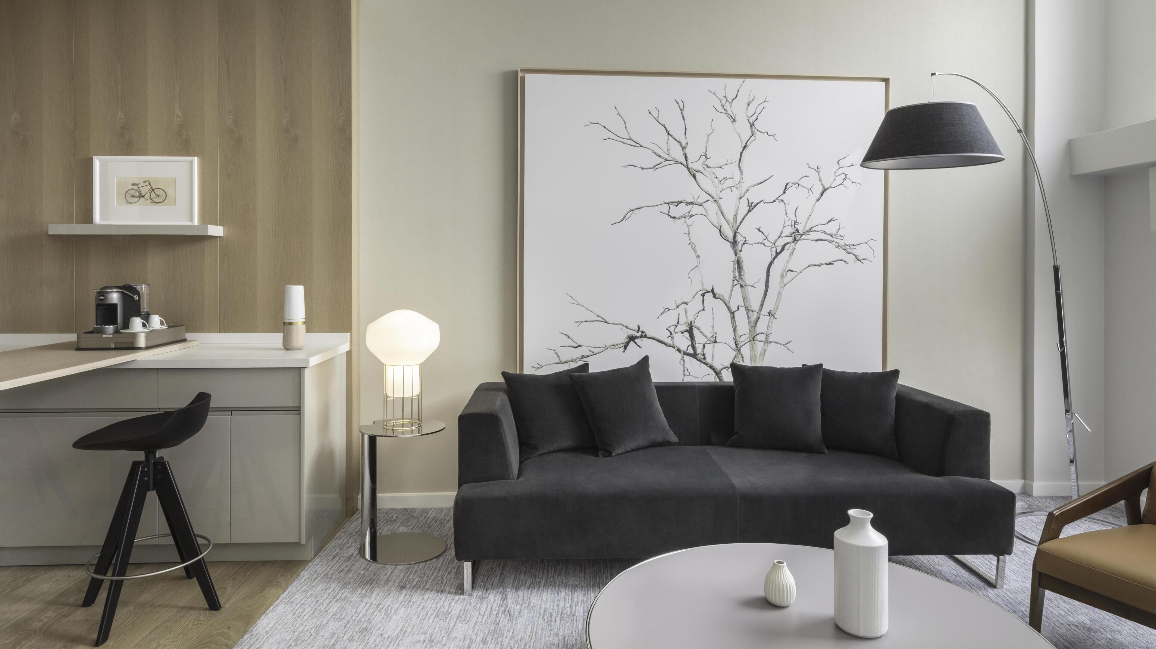 A modern living room with a dark grey sofa, a coffee machine, a framed artwork, and a floor lamp.