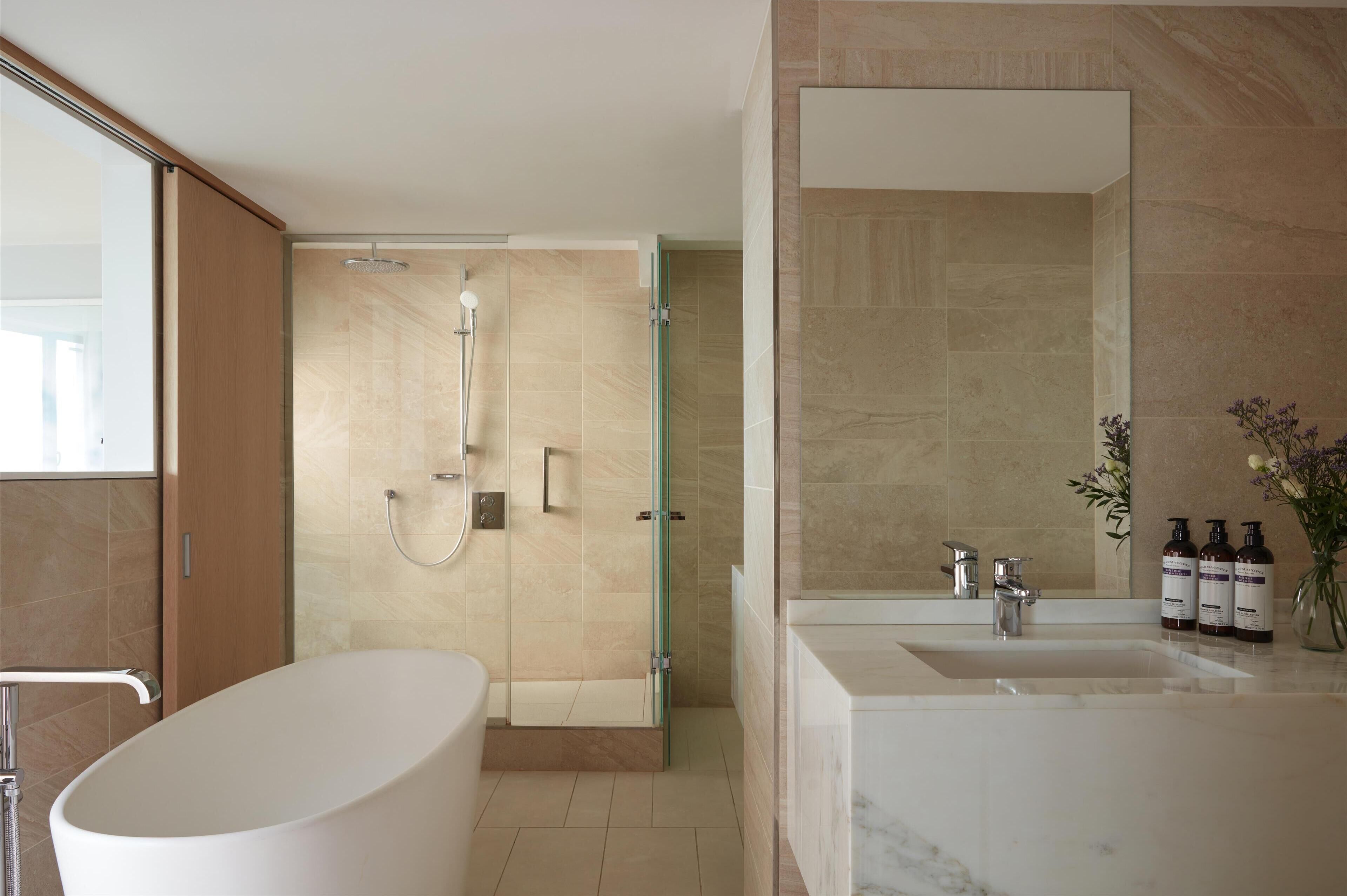 Un baño moderno con ducha de vidrio, una bañera independiente y un lavamanos con un espejo grande y artículos de aseo.