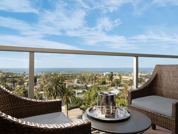 A modern bathroom with a large mirror, a marble countertop, and a view of a bedroom with a bed and a balcony. at Hotel La Jolla, Curio Collection by Hilton