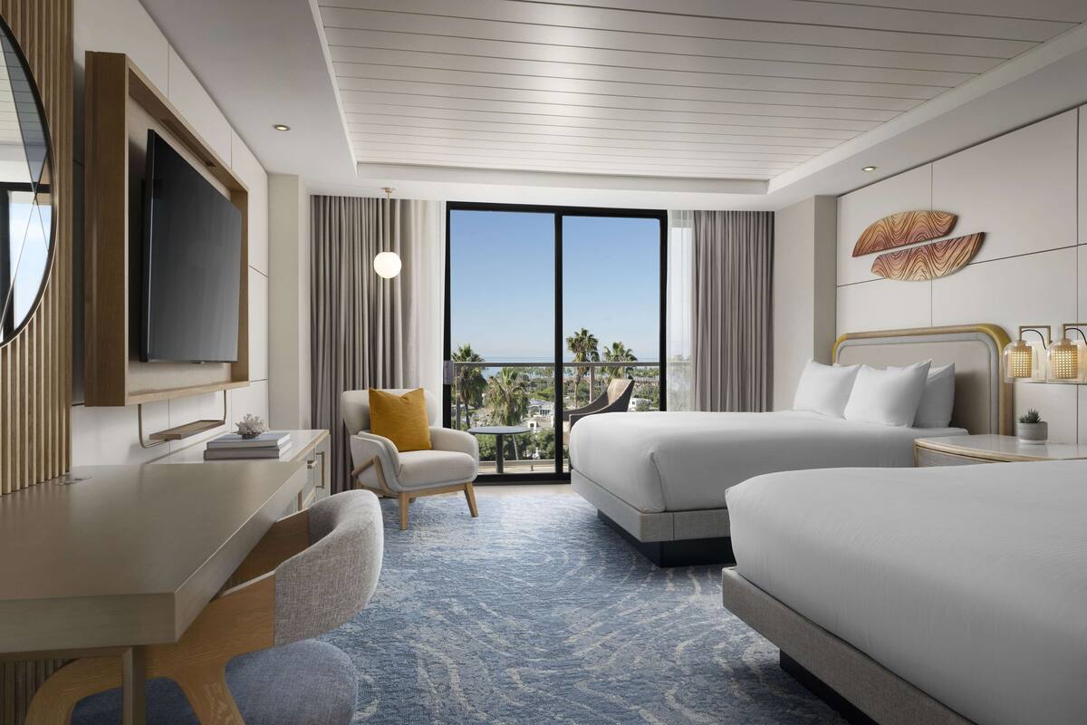 A hotel room with a large bed, a desk, a chair, a TV, and a view of the ocean.