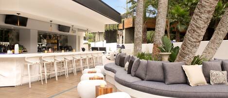 A modern outdoor seating area with a bar, white bar stools, and a curved sofa with cushions.