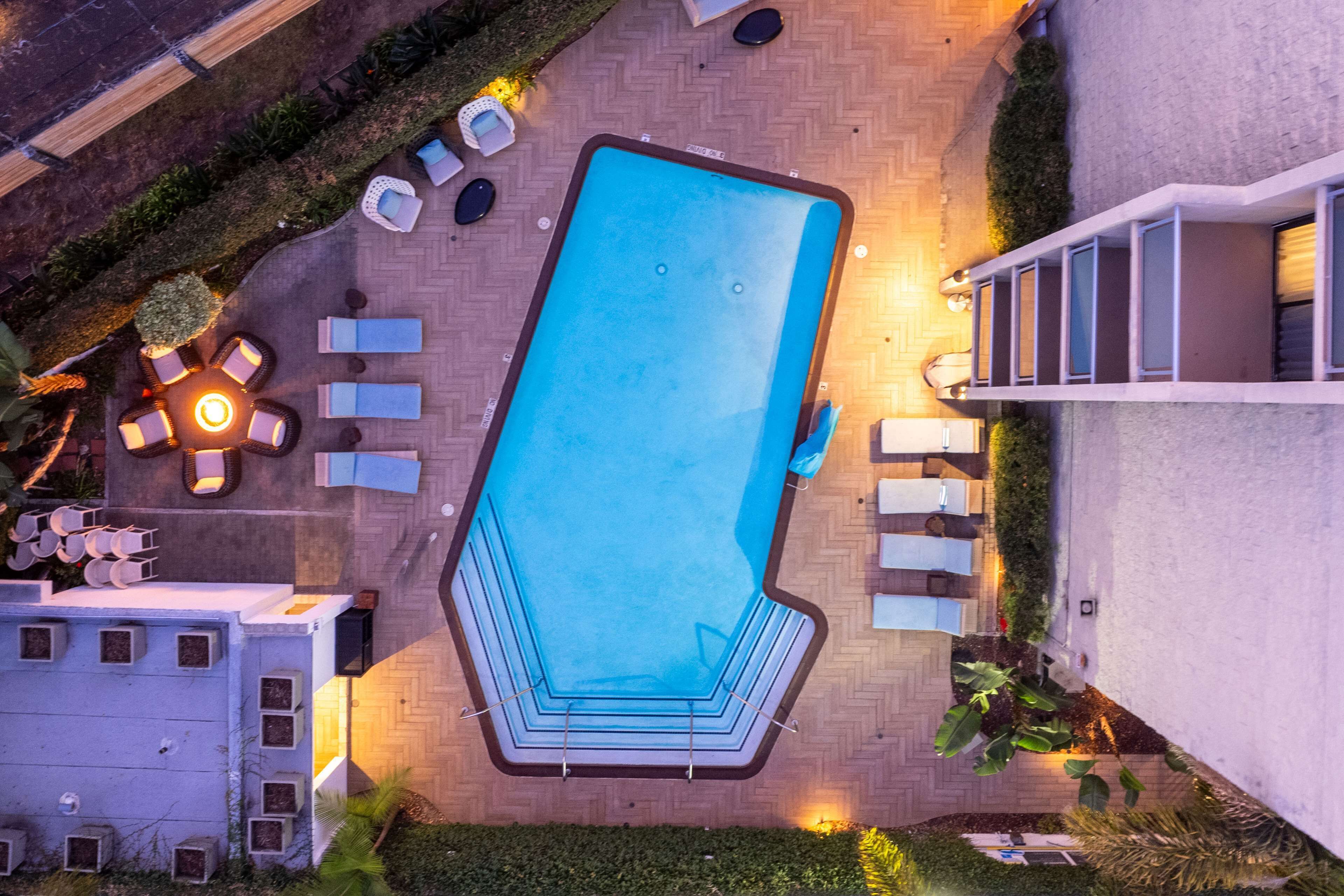 An aerial view of a swimming pool with a geometric shape, surrounded by lounge chairs and a small fire pit.