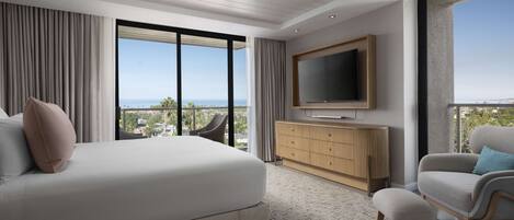 A modern hotel room with a large bed, a TV mounted on the wall, a seating area with a chair, and a view of the city through large windows.