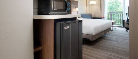 A compact hotel room with a bed, a refrigerator, a microwave, and a small table.
