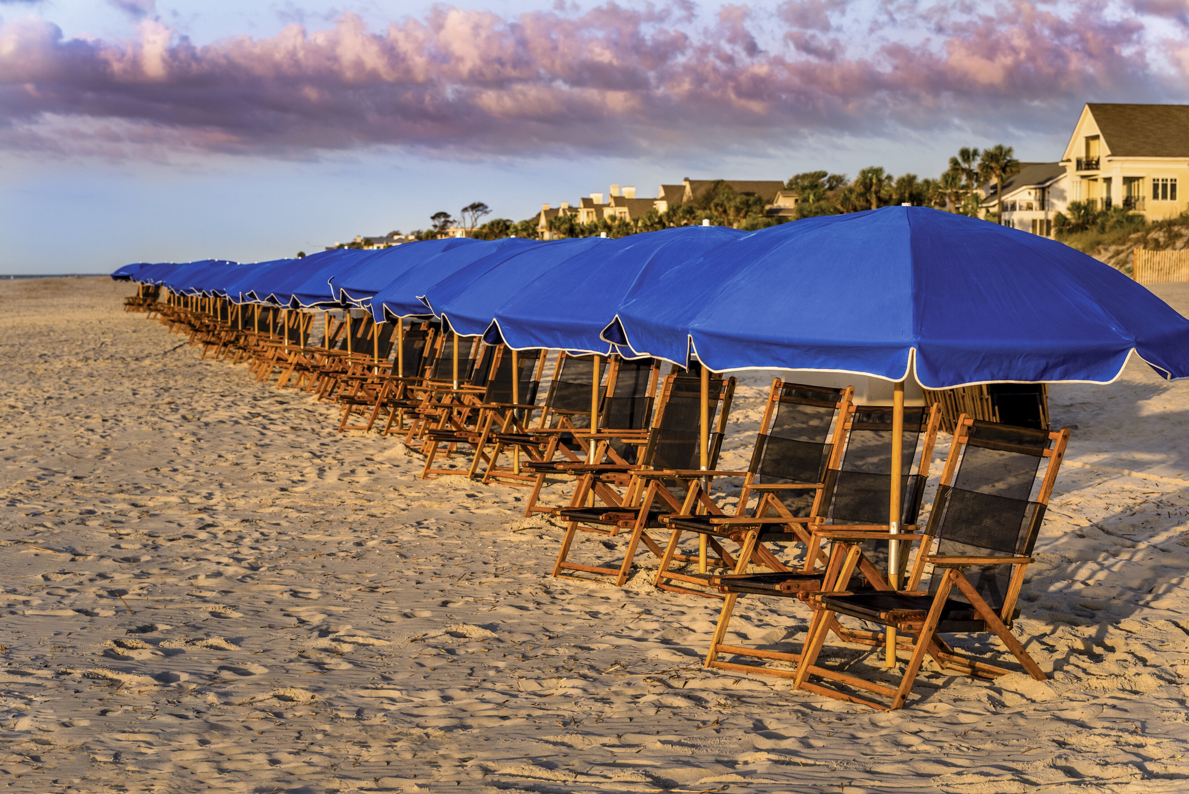 A beach with rows of wooden beach chairs and blue umbrellas.