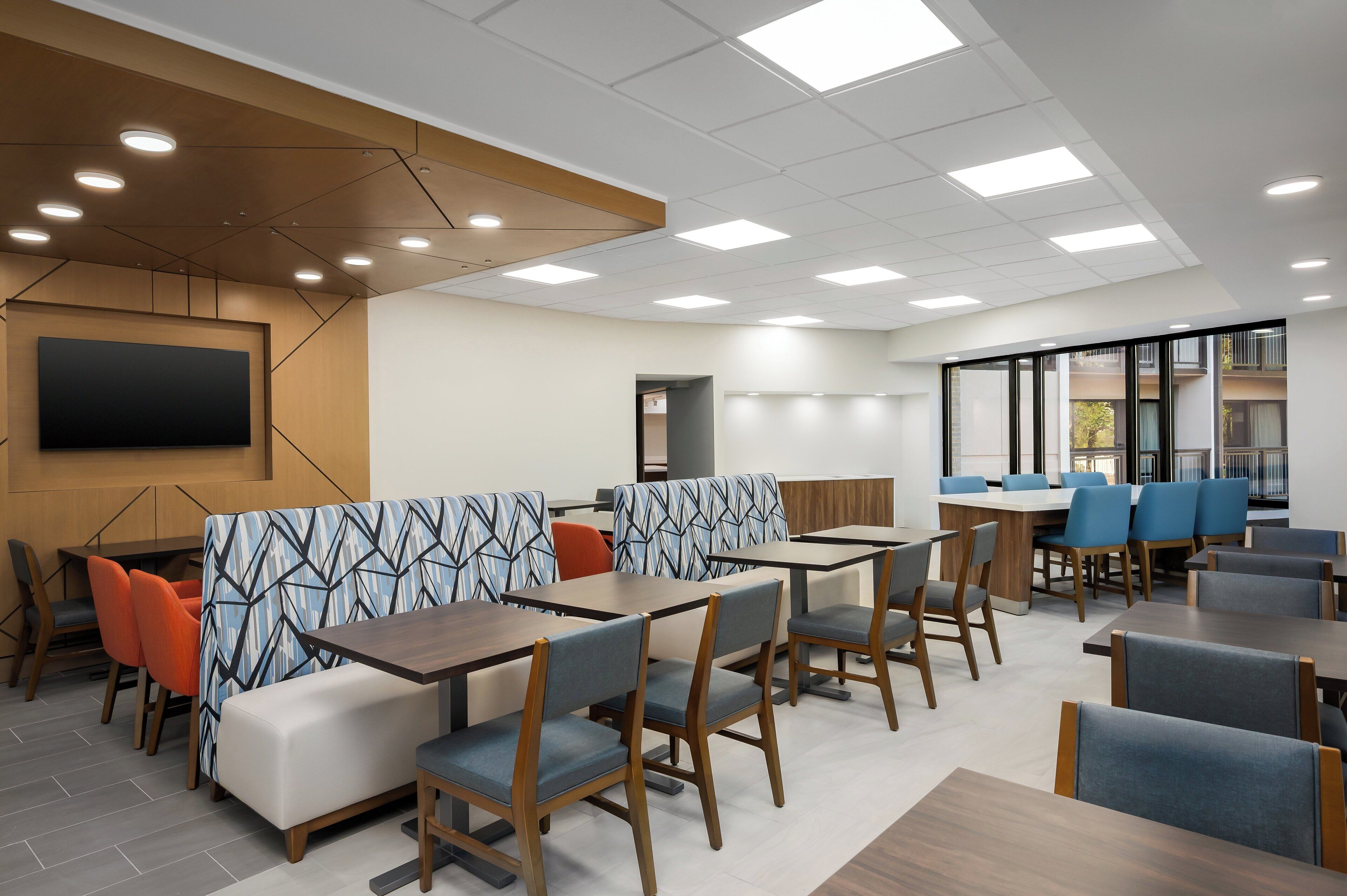 A modern dining area with booths and tables, recessed ceiling lights, and a large flat-screen TV on the wall.