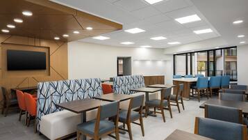 A modern dining area with booths and tables, recessed ceiling lights, and a large flat-screen TV on the wall.