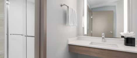 Un bagno moderno con cabina doccia in vetro, un lavandino bianco su mobile in legno e uno specchio grande.