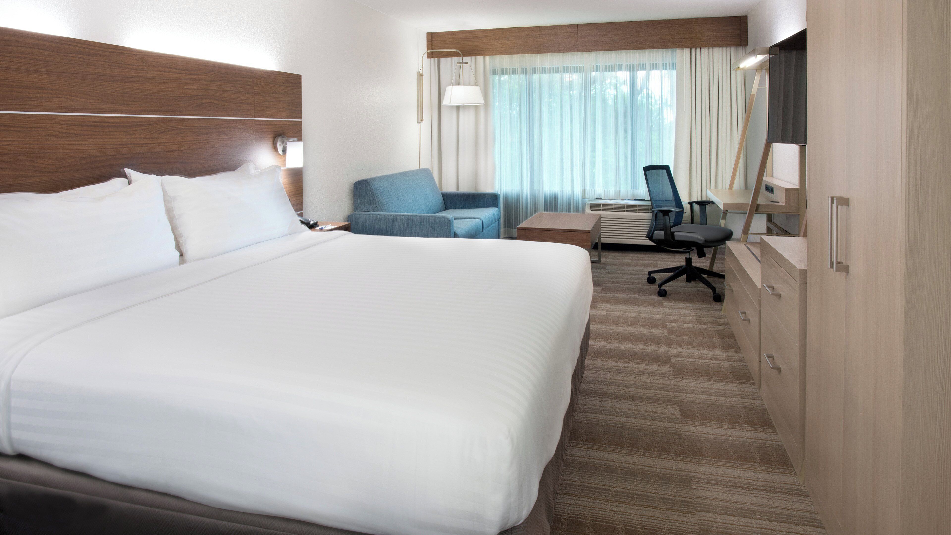 A hotel room with a large bed, a desk, a chair, and a mirror.