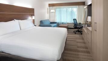 A hotel room with a large bed, a desk, a chair, and a mirror.