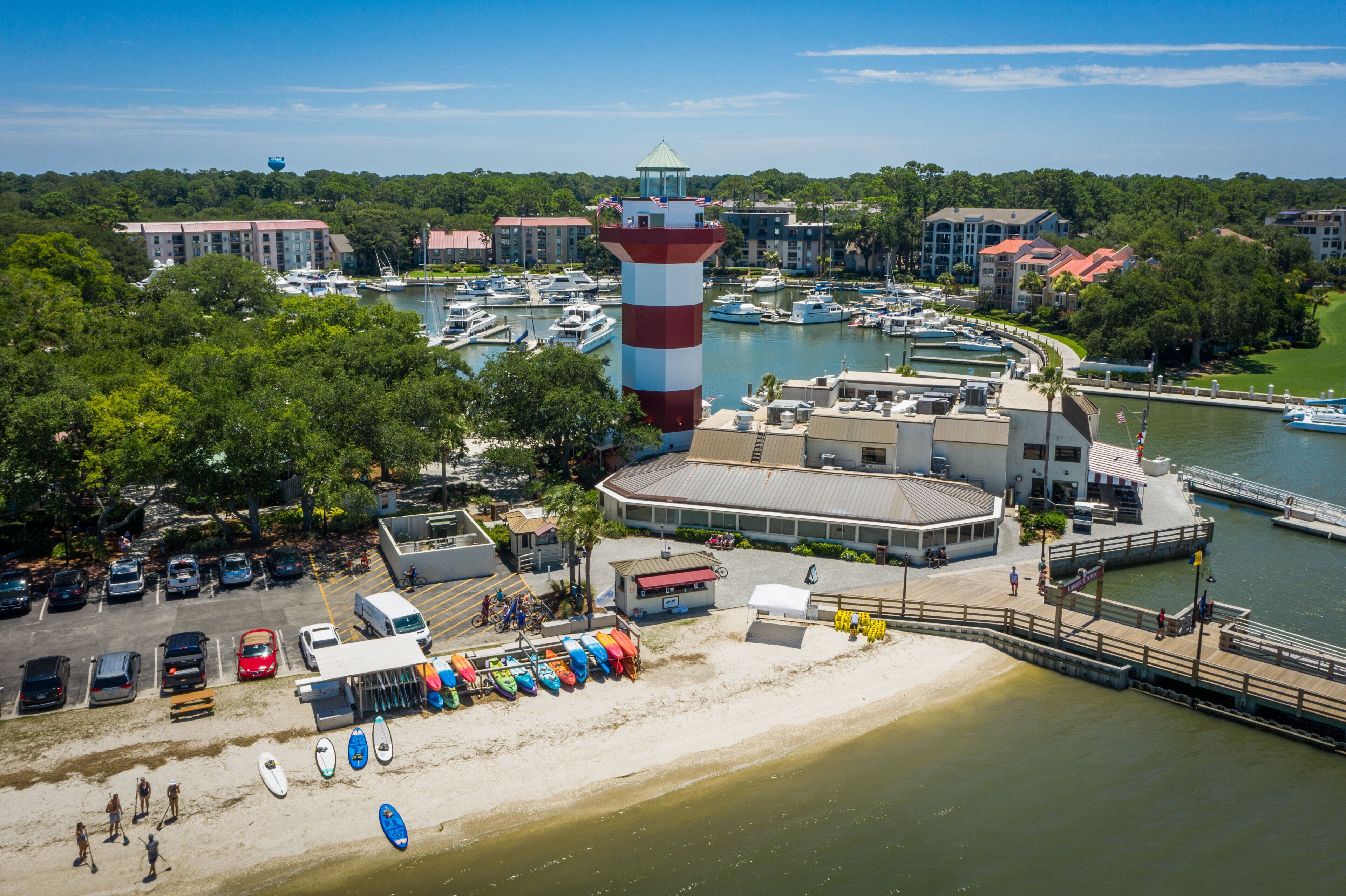 A marina with boats, a lighthouse, and a beach with paddleboards.