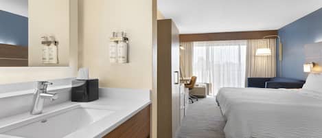A hotel room with a large bed, a bathroom with a sink and mirror, a desk, and a chair.