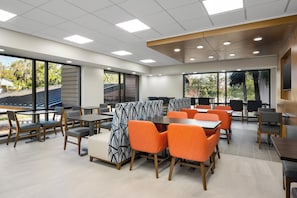 Un espace repas moderne, doté de tables et de chaises, de grandes fenêtres et offrant une vue sur l’extérieur.