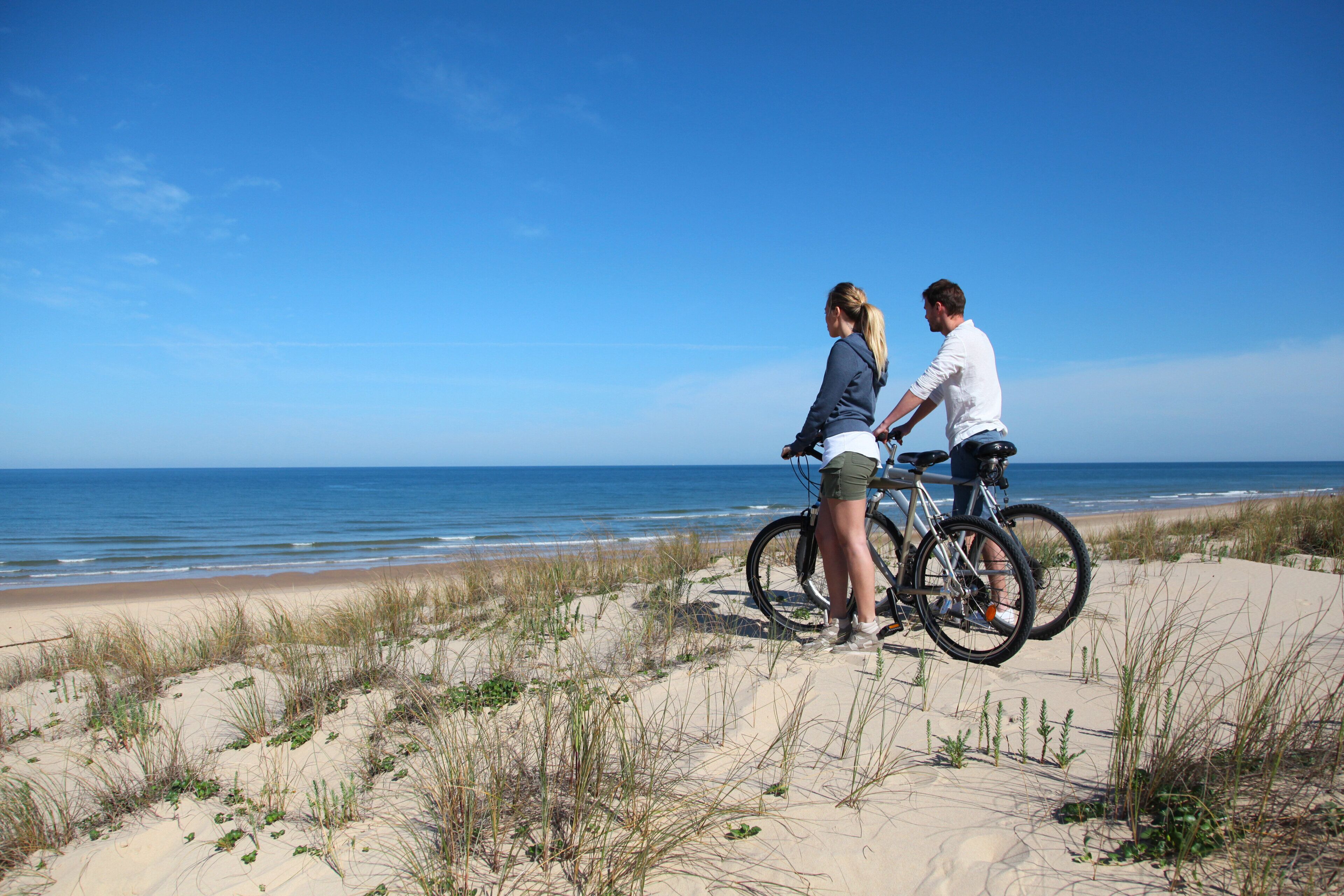 Two people on a sandy beach with a bicycle, overlooking the ocean.