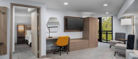 Una habitación de hotel moderna con un escritorio de madera, un espejo grande, un sofá cómodo y una televisión.