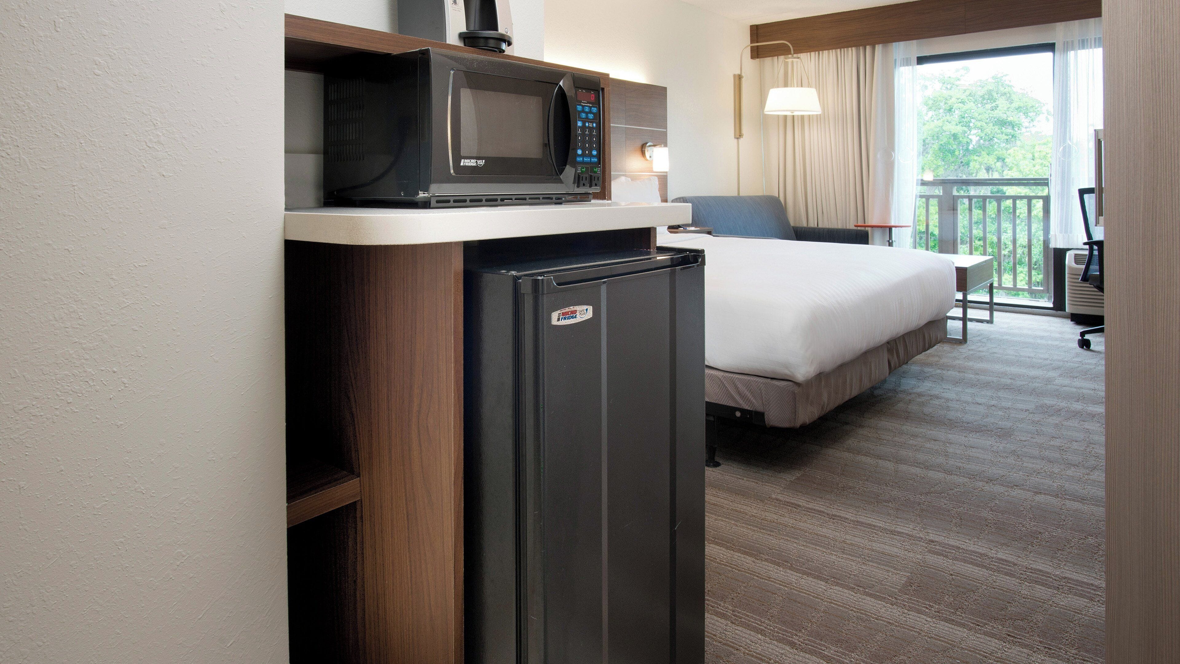 A compact hotel room with a bed, a small refrigerator, and a microwave on a shelf.