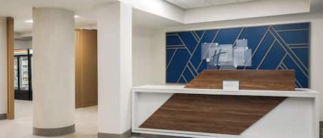 A reception desk with a blue and brown geometric wall design, a white counter, and a blue carpet.