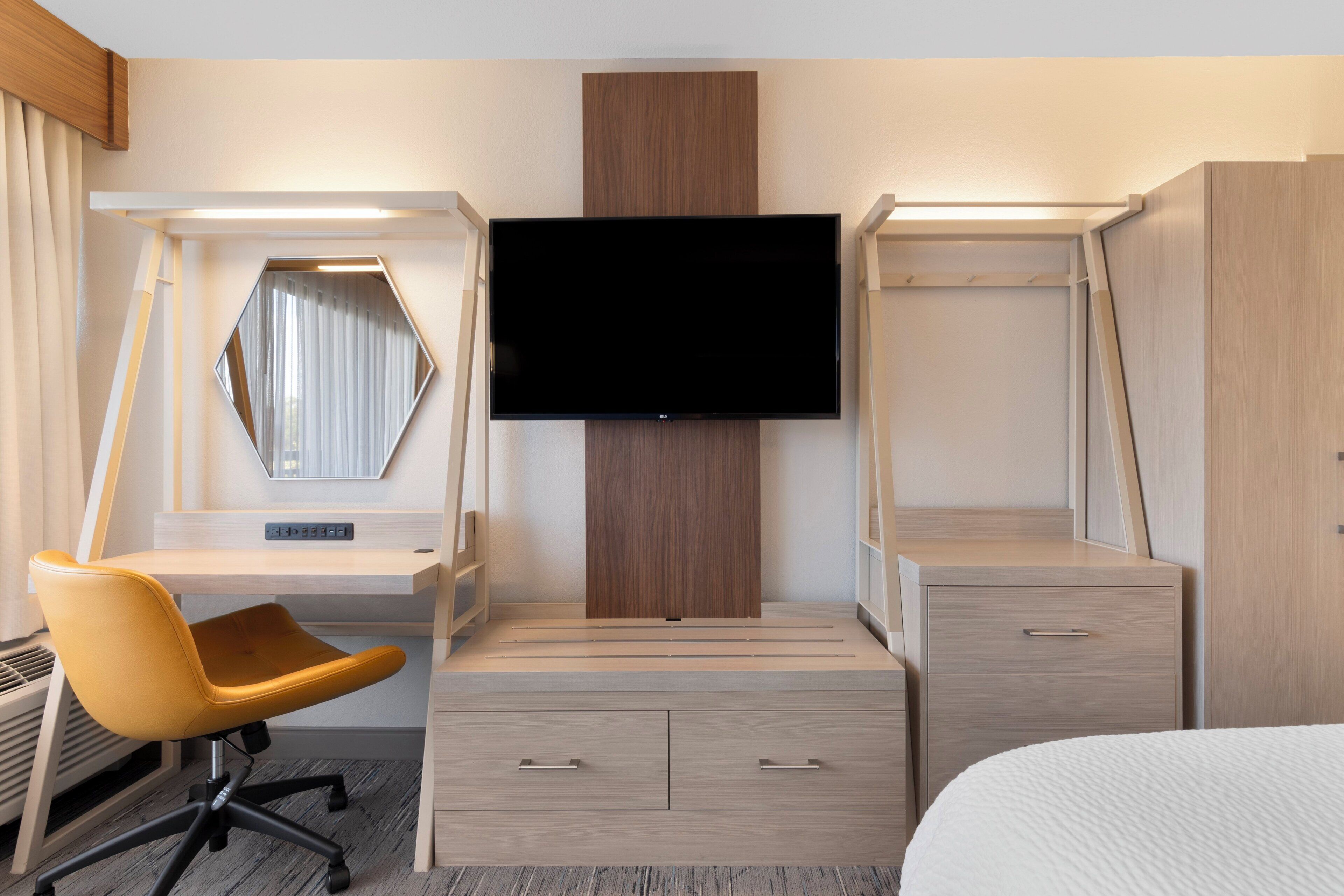 A hotel room with a bed, a desk with a chair, a television, and a wardrobe.