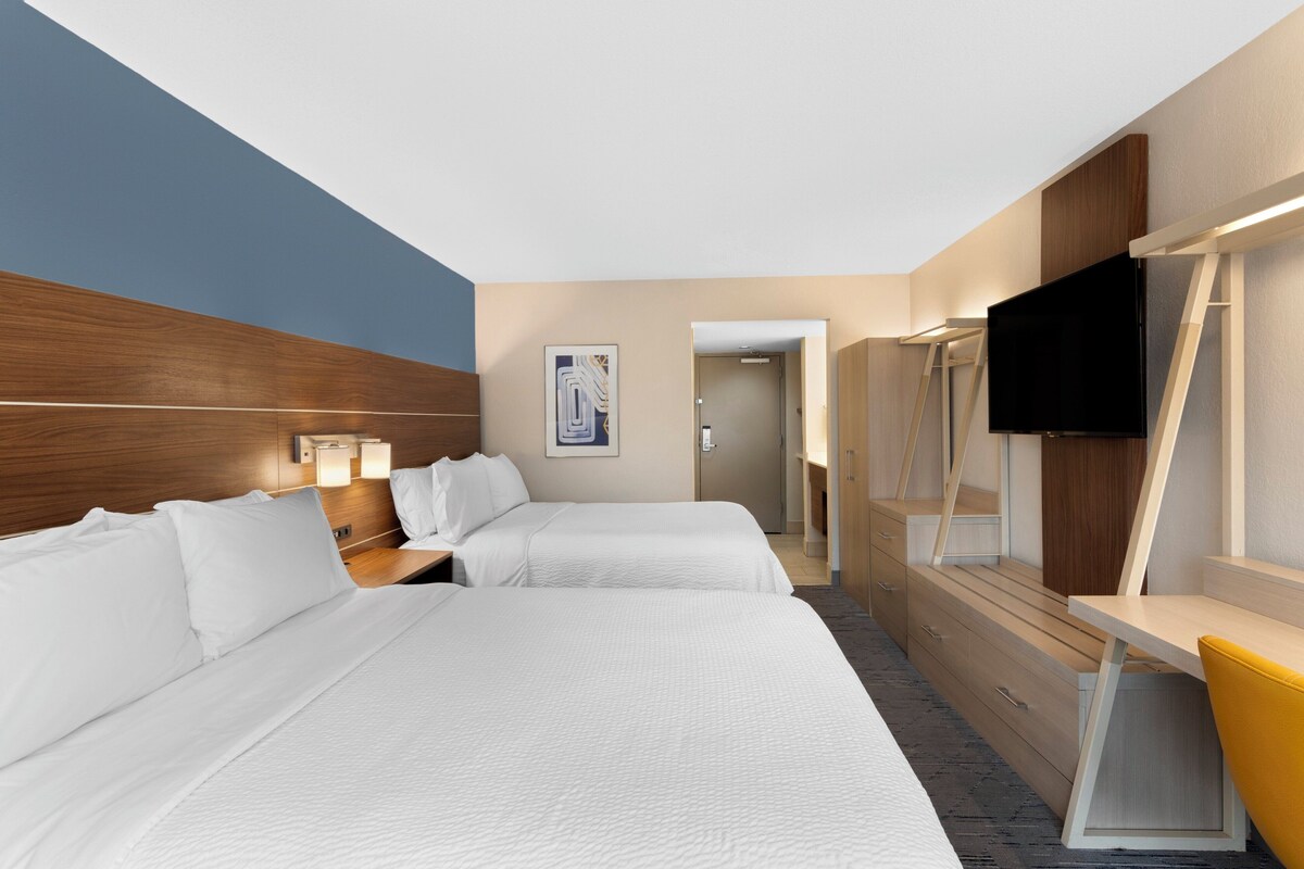Une chambre d’hôtel avec deux lits, un bureau, une télévision et une salle de bain visible à travers une porte ouverte.